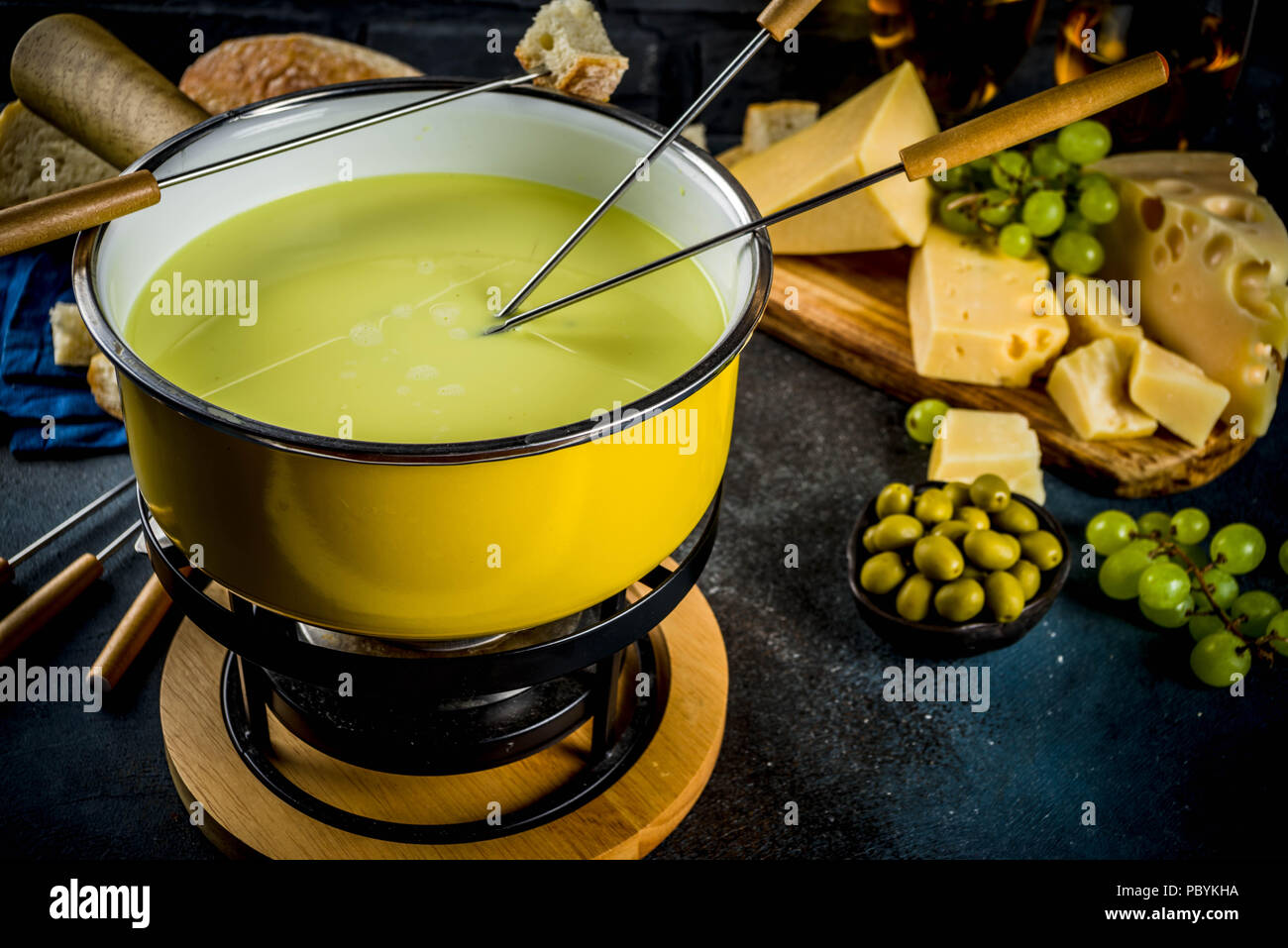 Gourmet Swiss fondue in traditional fondue pot, with forks, various cheeses, olives, bread and