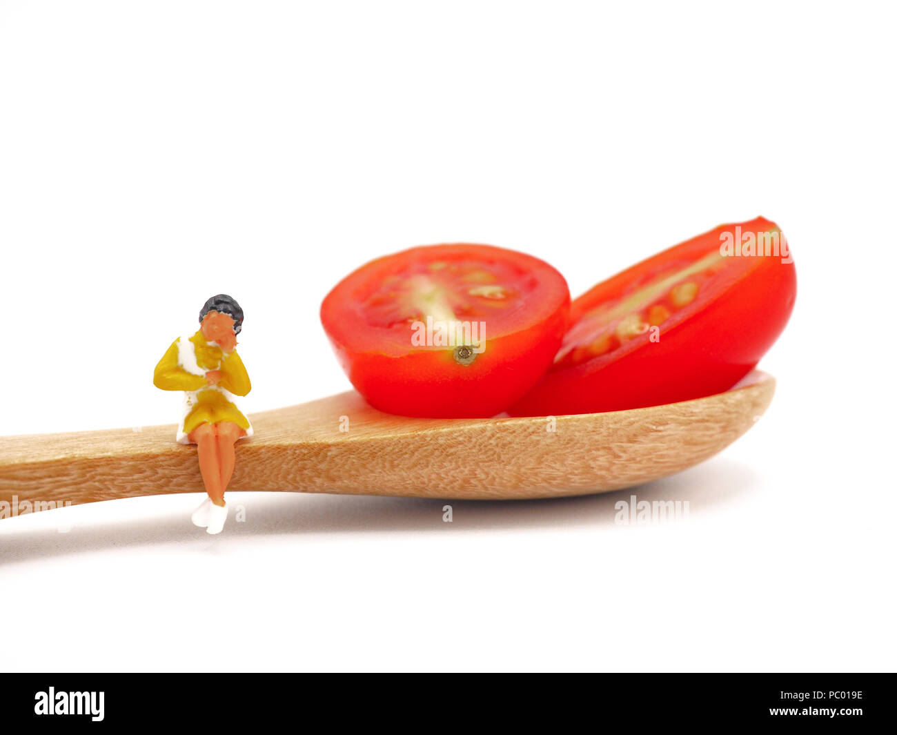 Miniature woman sitting on fresh grape or cherry tomato with wooden