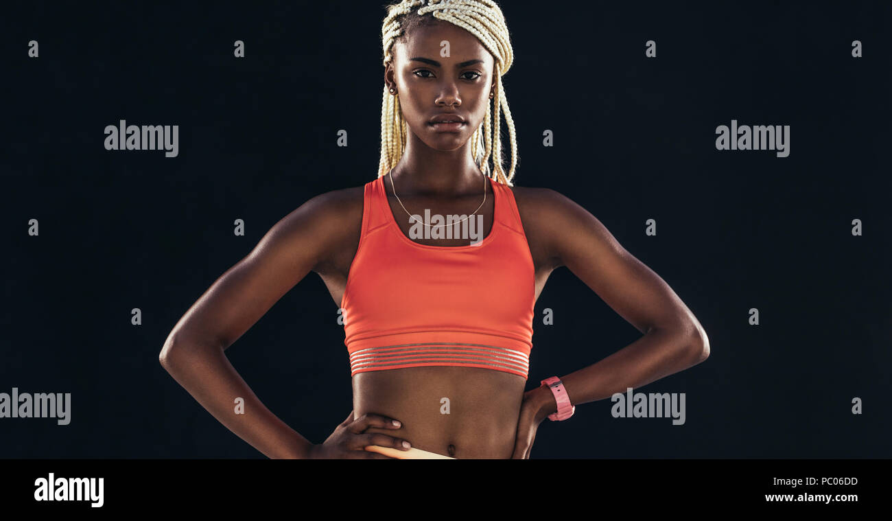 Portrait of a female athlete on a black background. Woman sprinter in fitness attire standing with hands on hip. Stock Photo