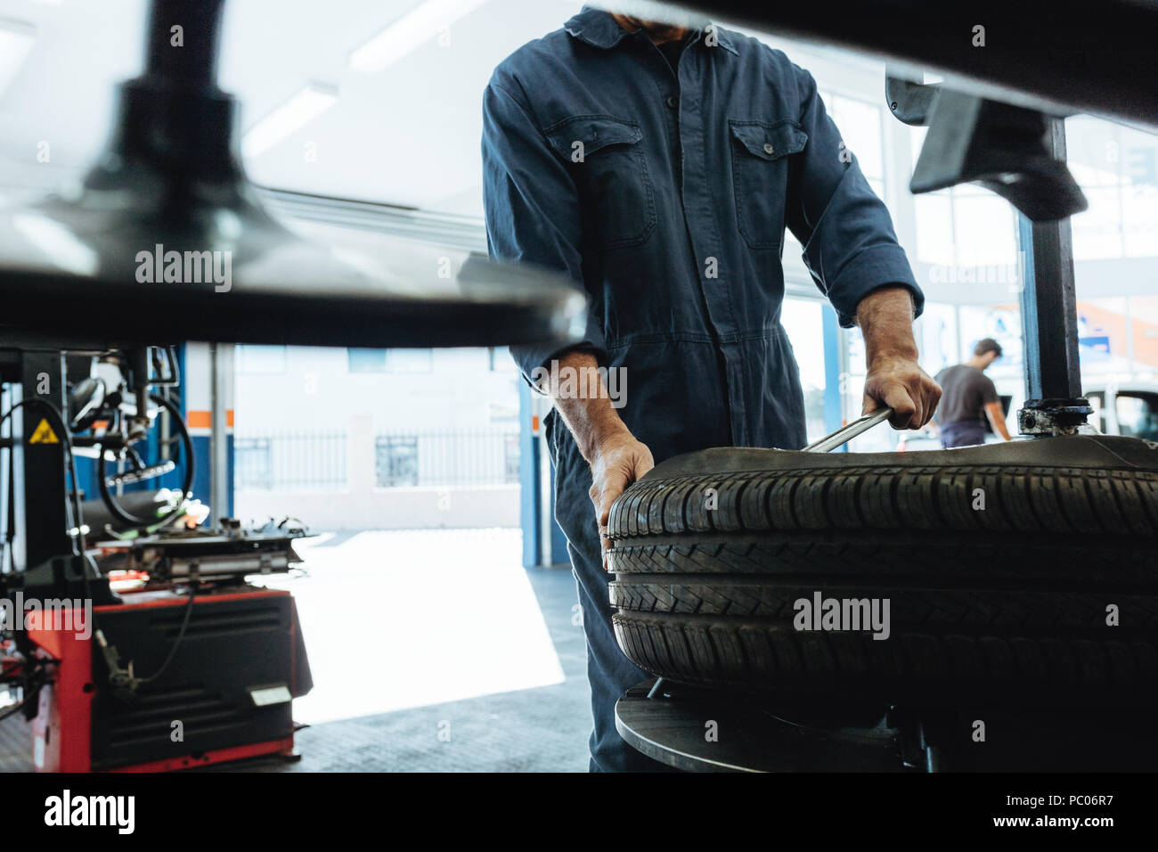 Mechanic removes car tire service station. Man working on machine for removing rubber from the wheel disc. Stock Photo