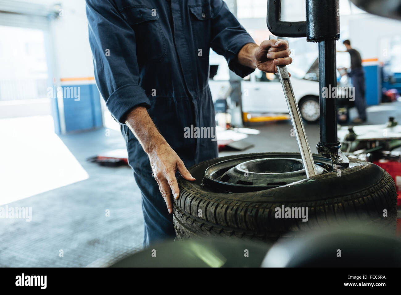 Mechanic changing car tire on a tire changing machine in workshop. Cropped shot of mechanic hands removing tire from disc on machine. Stock Photo