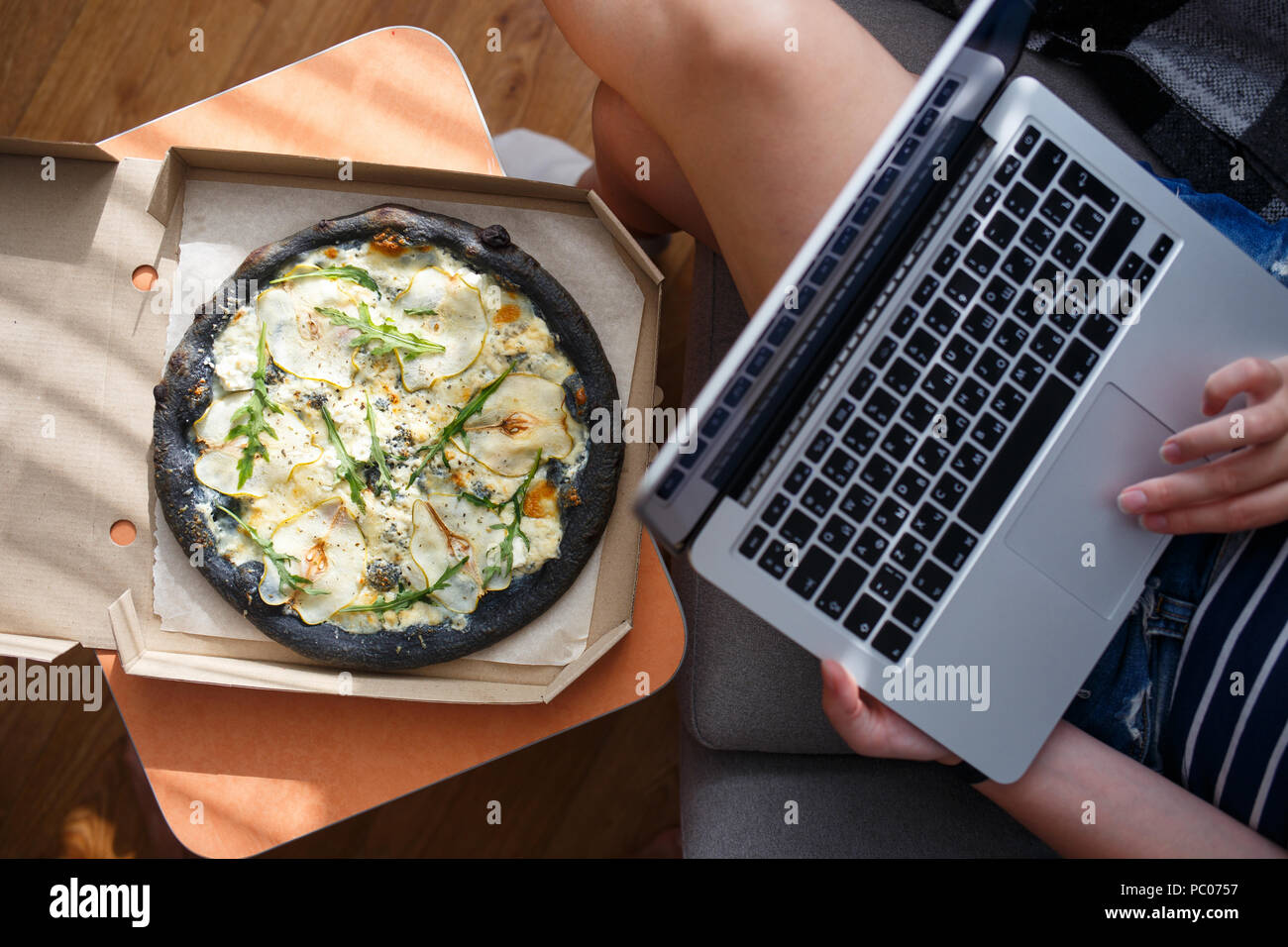 Young woman working on laptop with delivered pizza Stock Photo