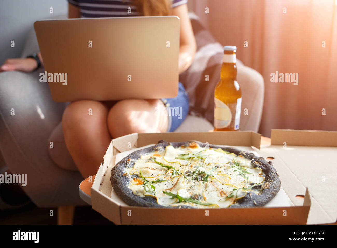 Young woman working on laptop with delivered pizza Stock Photo