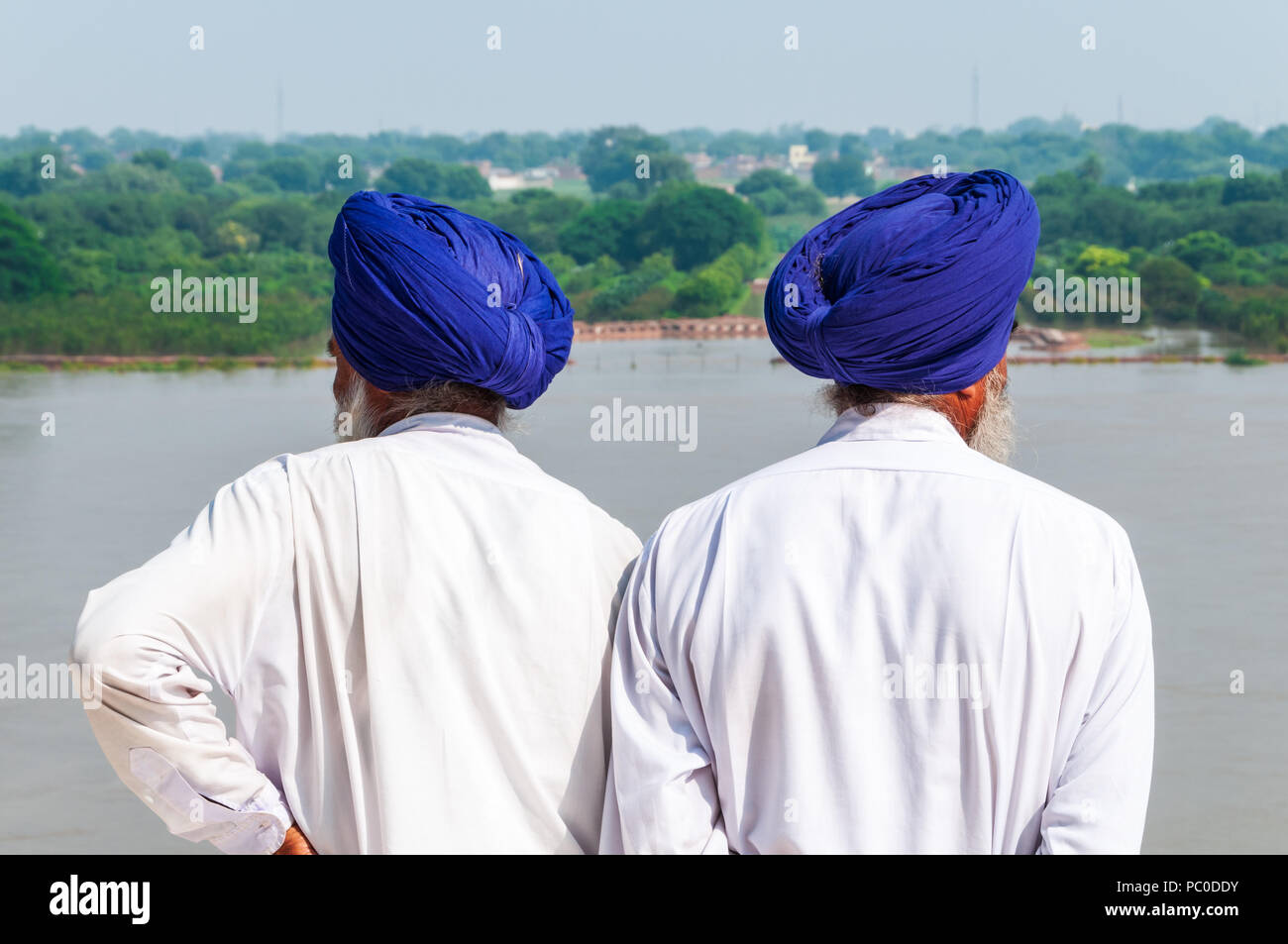 View from behind of two Indian Sikh men wearing identical blue turbans and looking in opposite directions away from the Taj Mahal in Agra, India Stock Photo