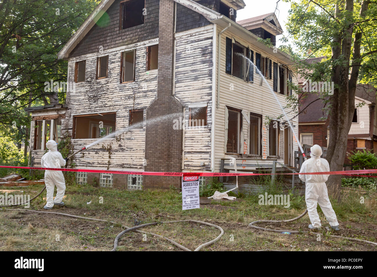 Detroit, Michigan - Using protective clothing to guard against asbestos exposure, workers demolish an abandoned house. They spray water on the buildin Stock Photo