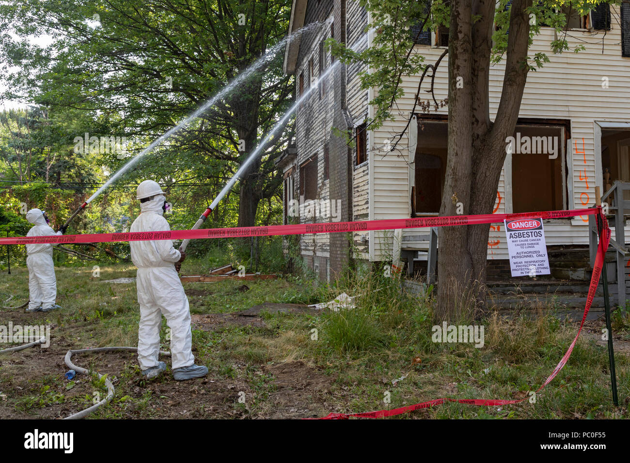 Detroit, Michigan - Using protective clothing to guard against asbestos exposure, workers prepare to demolish an abandoned house. They spray water on  Stock Photo