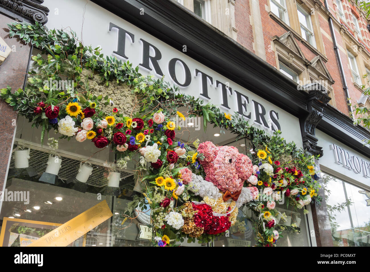 A floral entrance surrounds Trotters Childrenswear and Accessories store on Kensington High Street, London, UK Stock Photo