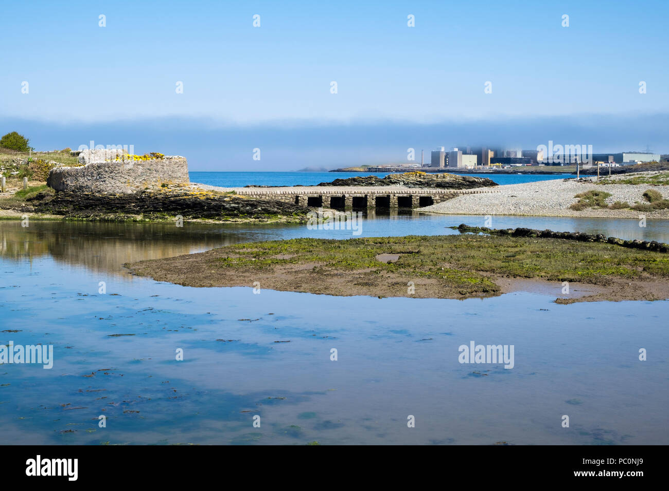 View across Cemlyn Bay tidal pool to footbridge and old Wylfa Nuclear Power Station in sea mist. Cemaes, Isle of Anglesey, Wales, UK, Britain Stock Photo