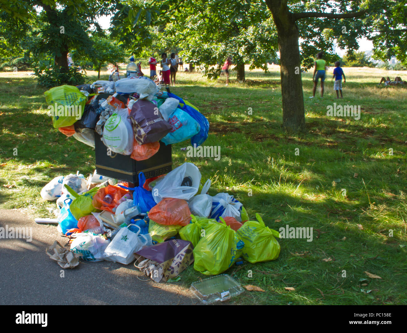 Rubbish bin overflowing in a park, people in background Stock Photo
