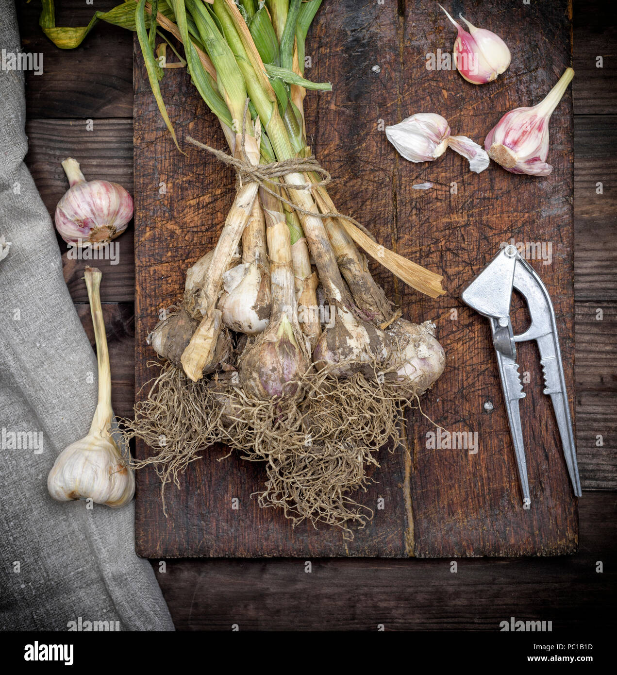 bunch of fresh young garlic tied with a rope on a brown wooden board, top view Stock Photo