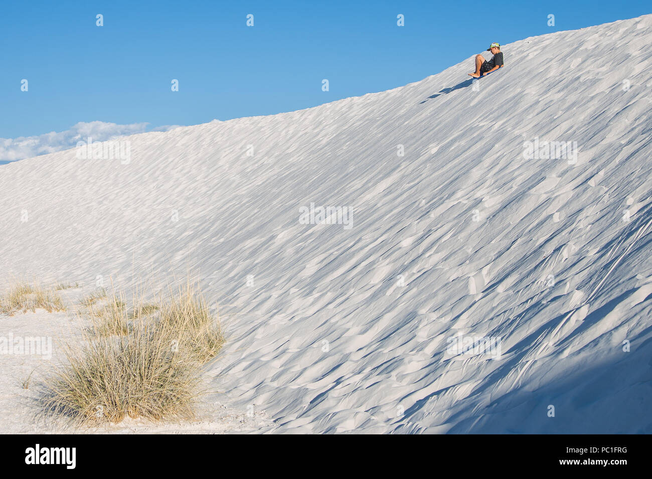 A caucasian boy sleds down a steep white sand dune in White Sands National Monument. Stock Photo