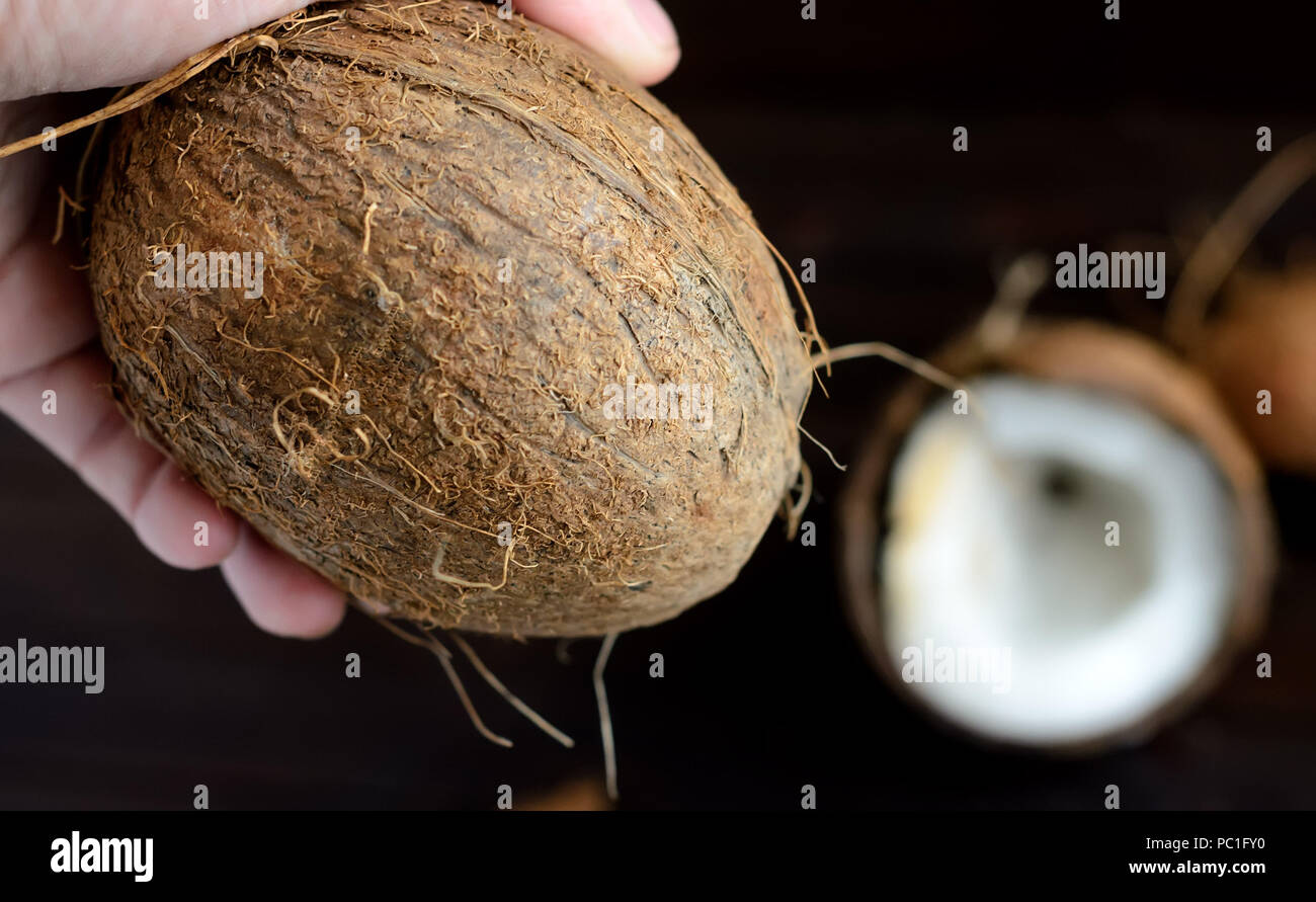 Hand holding a whole coconut on wooden background. .On the right half of the coconut in the bokeh. Stock Photo