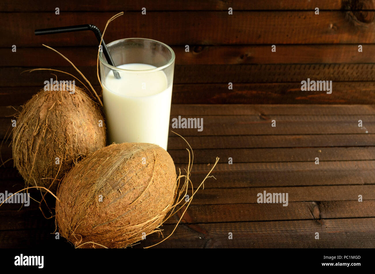 A glass of coconut milk and two whole coconuts on wooden background. Copyspace right. Stock Photo