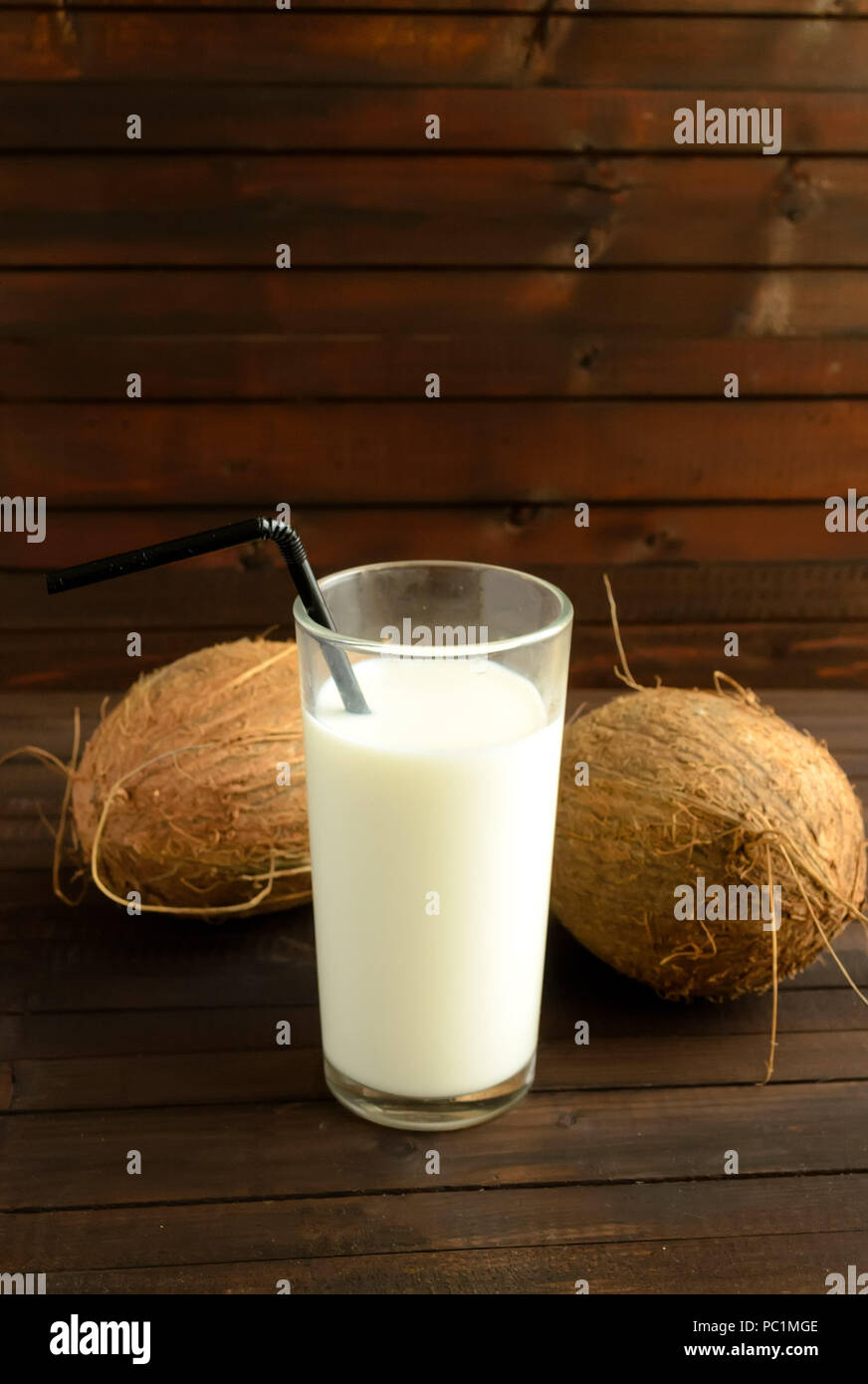 A glass of coconut milk and two whole coconuts on wooden background.Copyspace top. Stock Photo