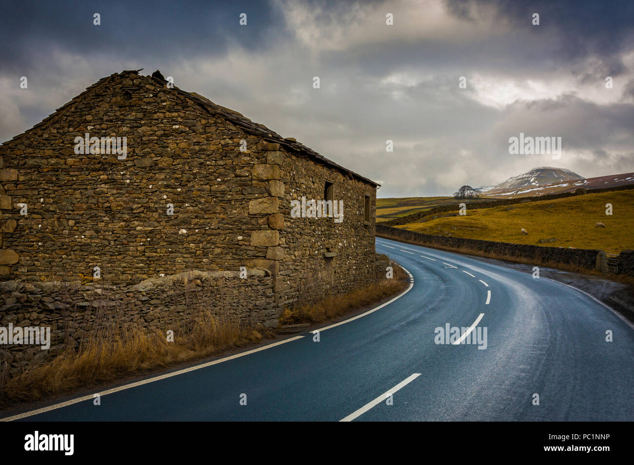 A barn on a blind bend on a winding road leading towards Pen-Y-Ghent seen in the distance. Stock Photo