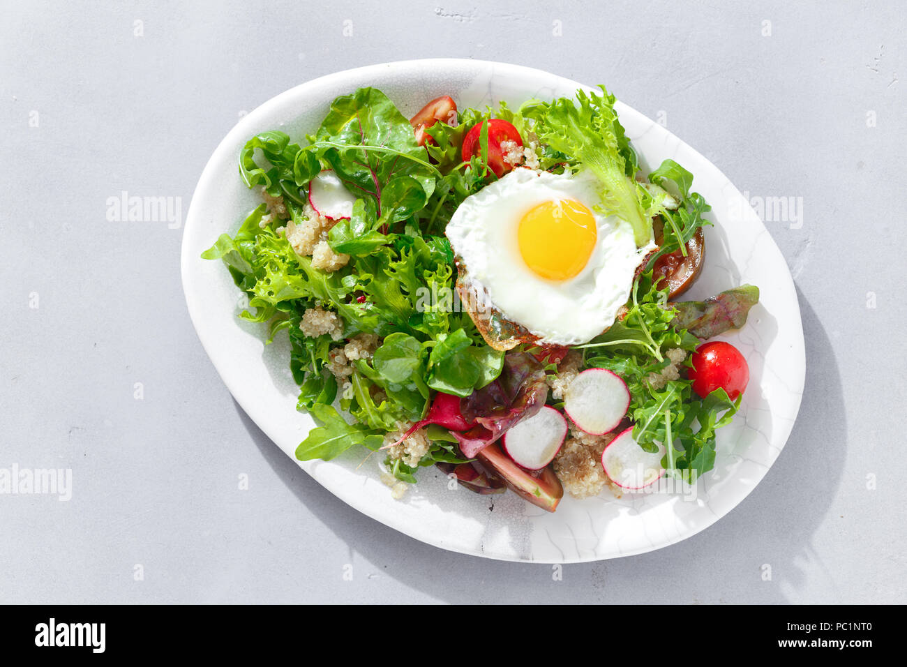 Plate fresh salad with quinoa and fried egg on gray concrete background. Healthy food clean eating Stock Photo