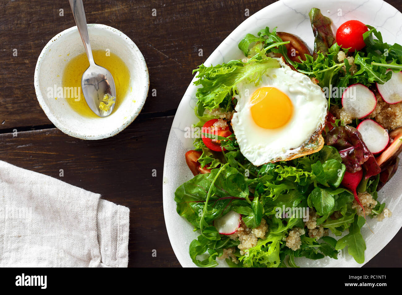 Plate fresh salad with white quinoa, fried egg and sauce on wooden table. Healthy food clean eating Stock Photo