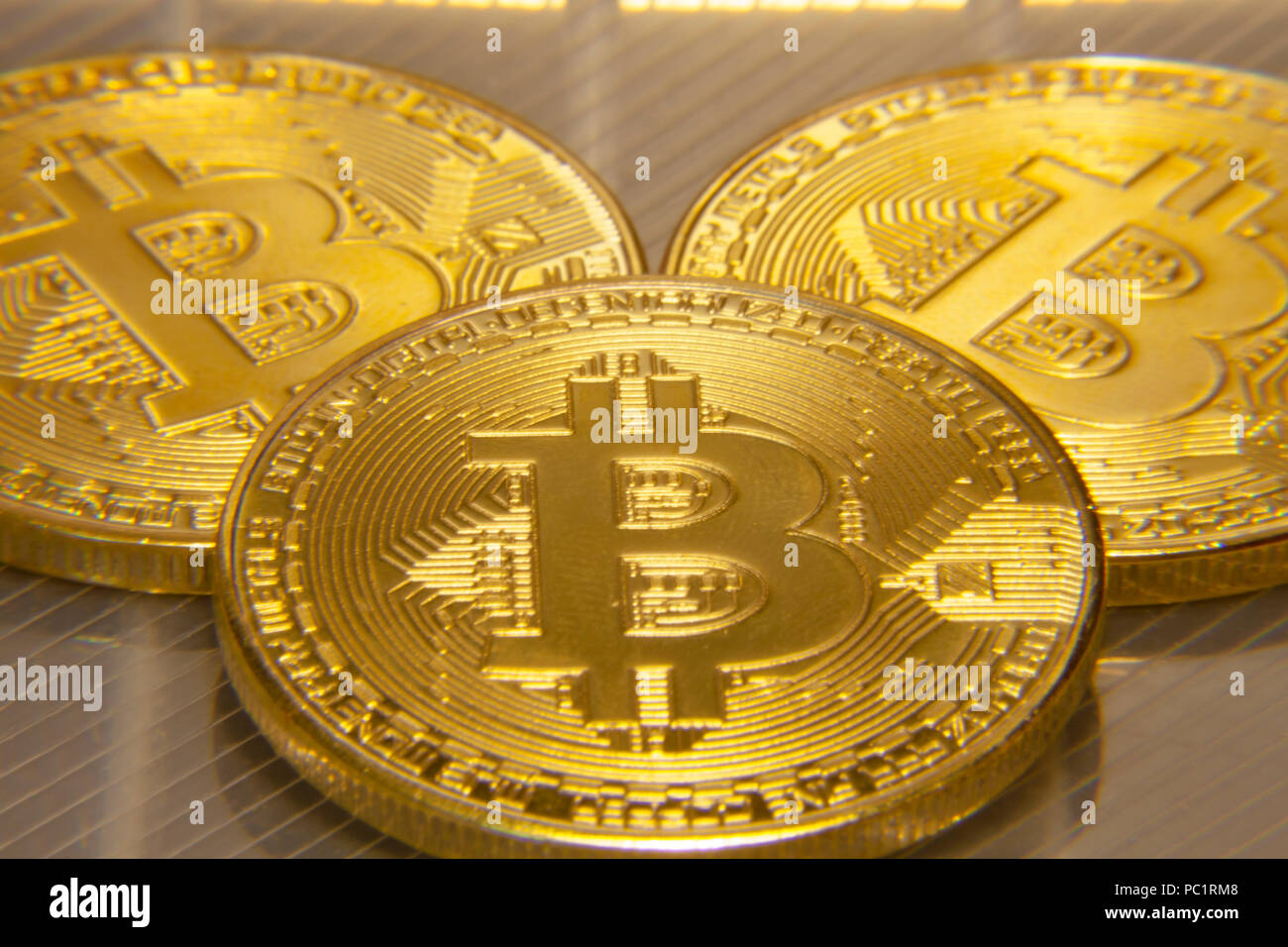 Macro close-up shot: three physical golden bitcoins (digital virtual crypto-currency) on a semi-transparent surface. Stock Photo