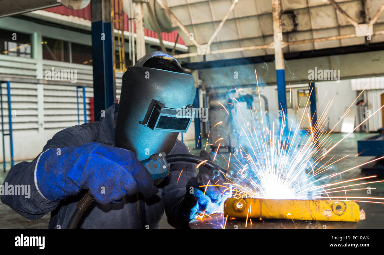 Worker is welding metal part with protective work wear Stock Photo