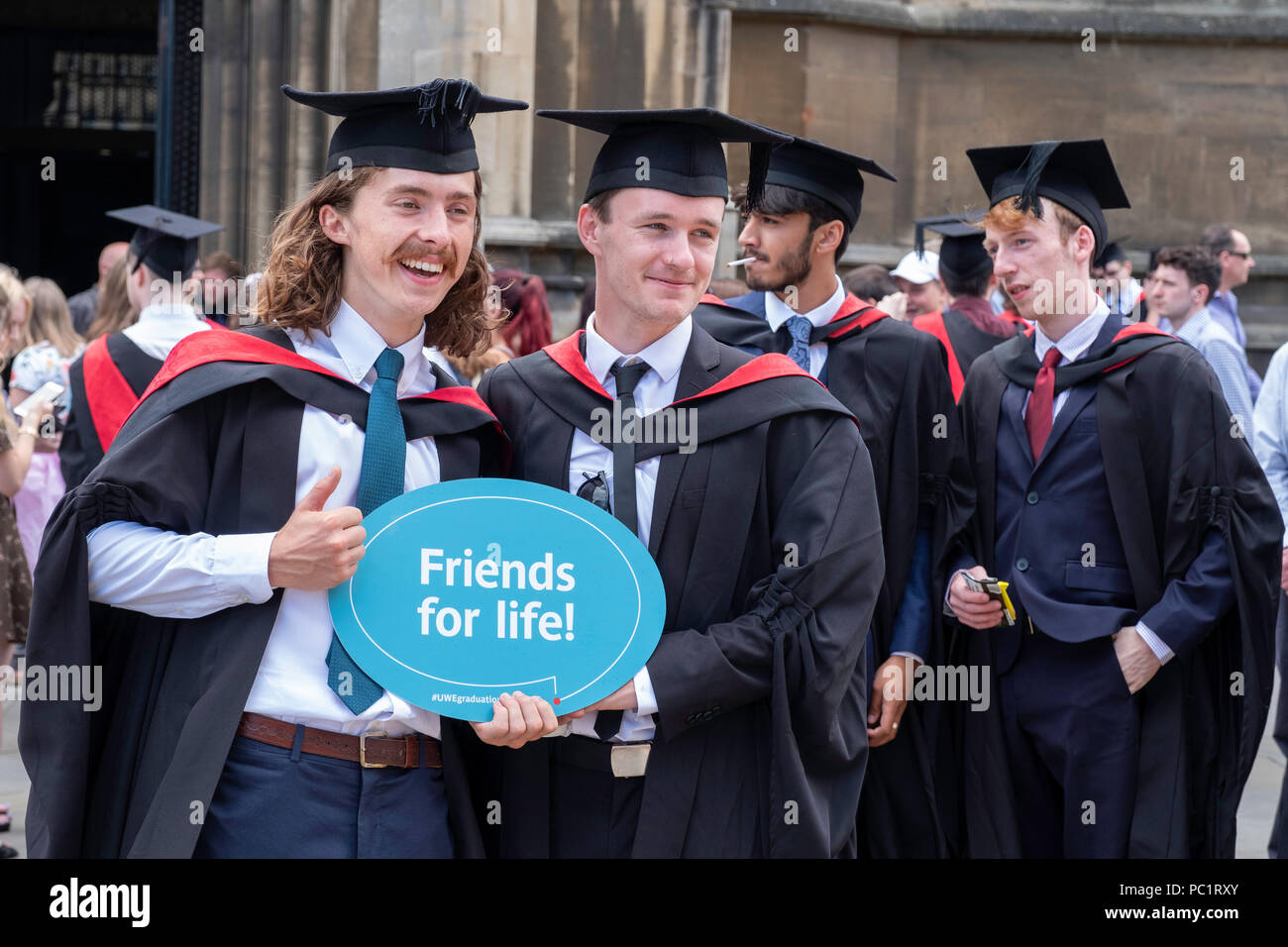Crowd of young men celebrating graduation holding sign,'Friends for Life' after graduation ceremony in Bristol, England YK. Stock Photo