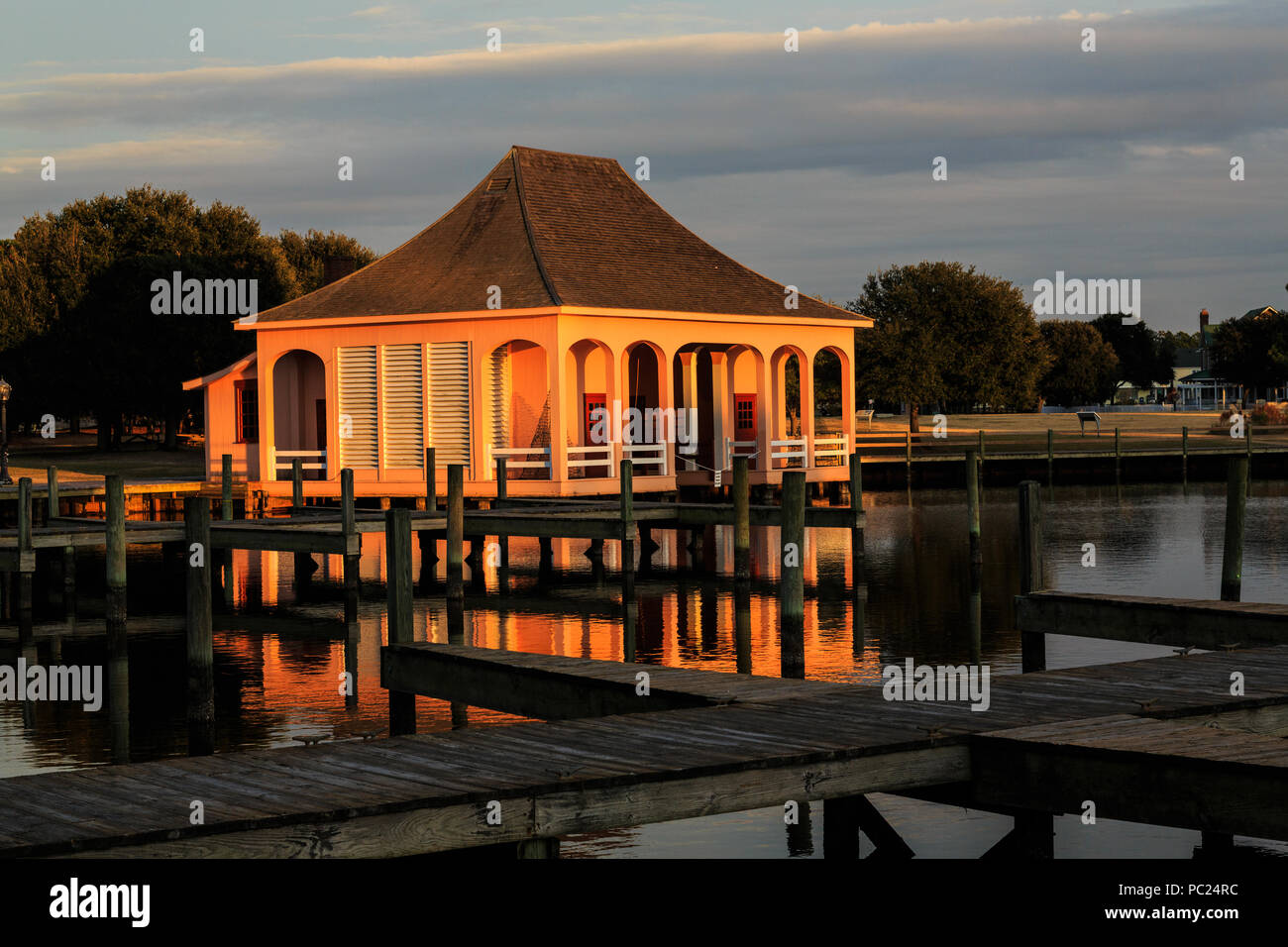 A golden 'magic hour'  sunset bathes a solitary boathouse, and its reflection, in a darker marina, Whalehead Club, Corolla, Outer Banks, NC Stock Photo