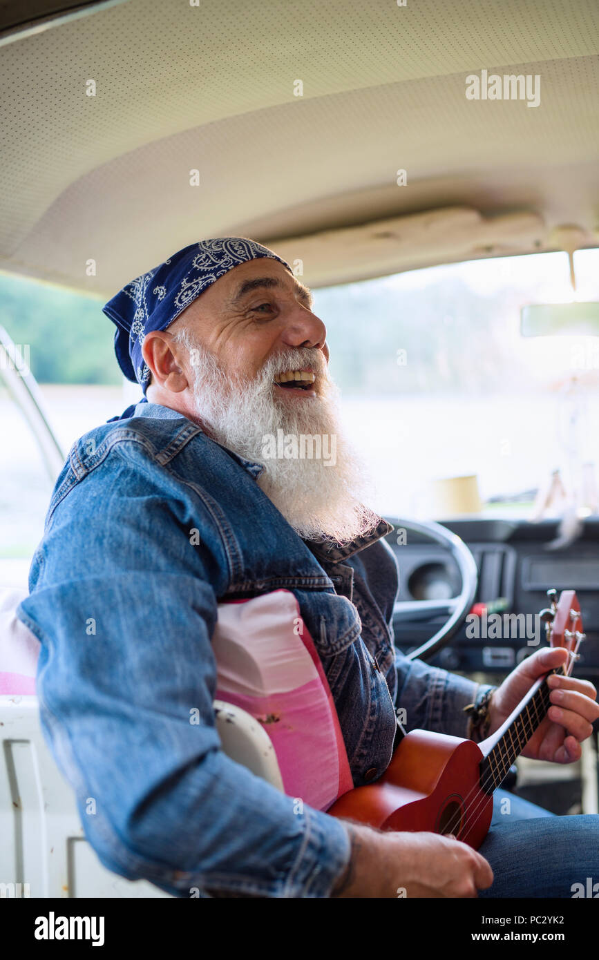 An old hipster sitting in a van playing ukulele Stock Photo Alamy