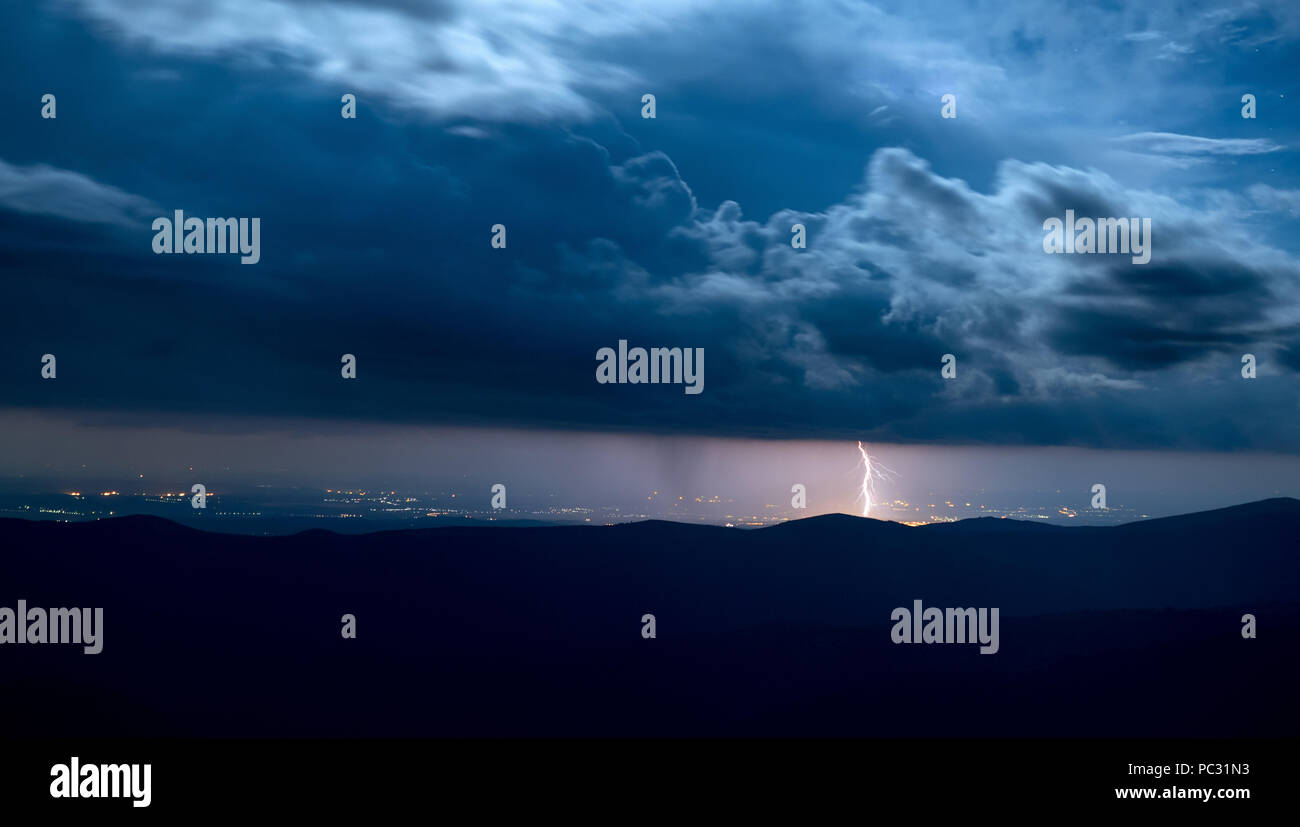 Lightning striking over a town in the mountains at night Stock Photo ...
