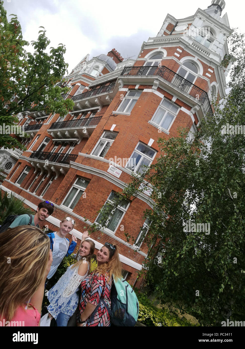 Tourists pose for photos on Abbey Road, opposite the famous studios, July 2018. The sign can be seen on the building behind. Stock Photo