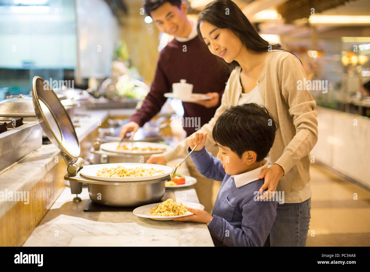 Cheerful young Chinese family taking food from buffet table Stock Photo ...
