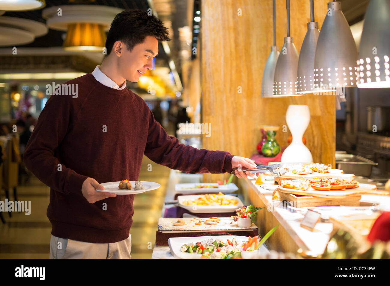 Cheerful young Chinese man taking food from buffet table Stock Photo