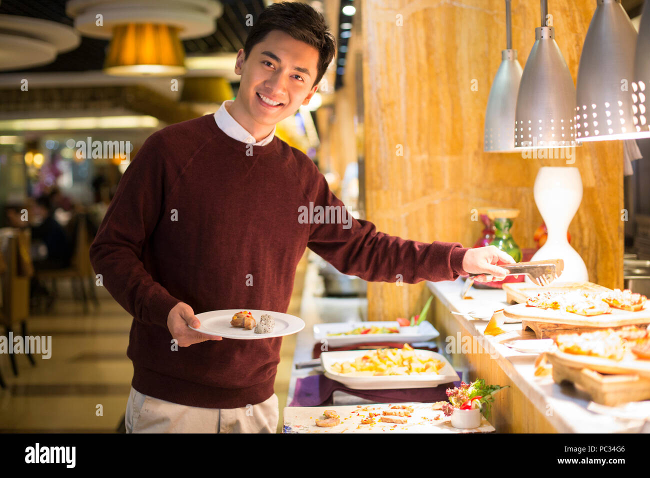 Cheerful young Chinese man taking food from buffet table Stock Photo