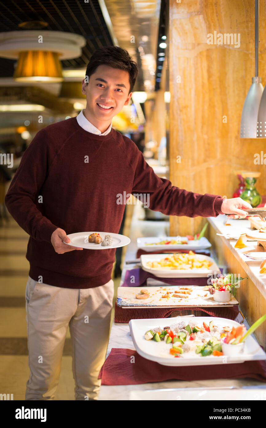https://c8.alamy.com/comp/PC34KB/cheerful-young-chinese-man-taking-food-from-buffet-table-PC34KB.jpg
