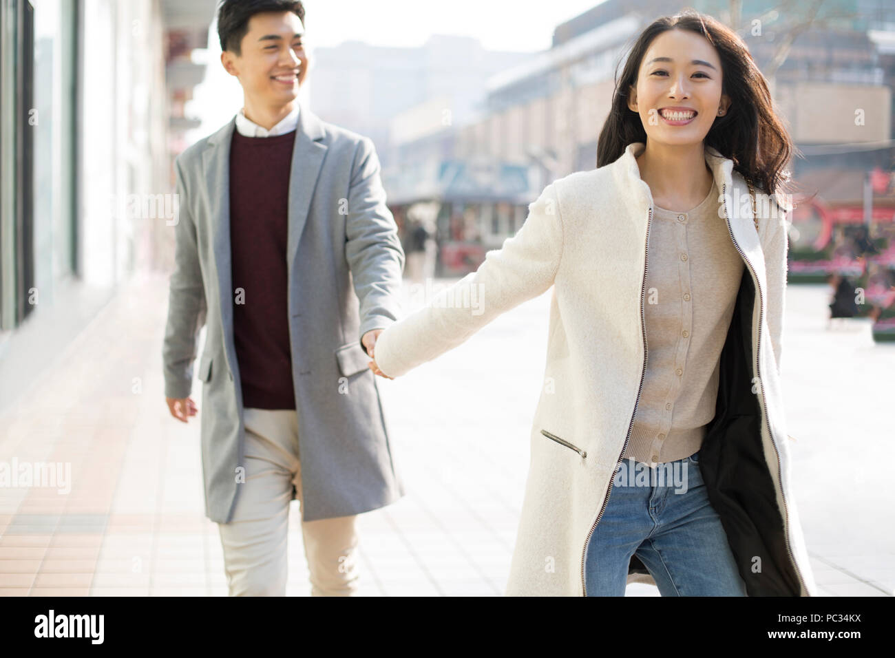 Cheerful young Chinese couple holding hands walking Stock Photo - Alamy