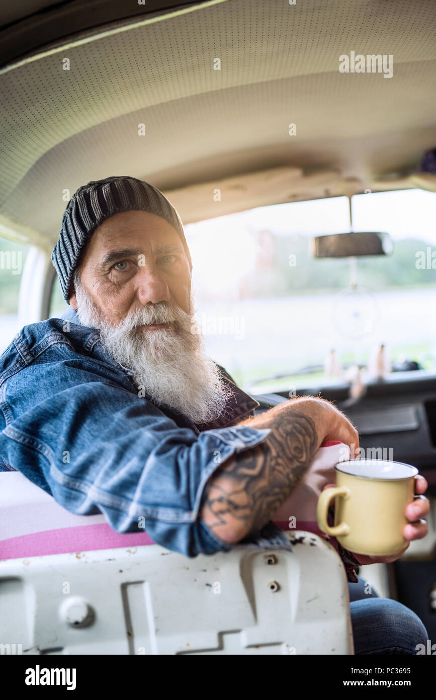 Portrait of an old hipster sitting in a van looking at camera Stock Photo