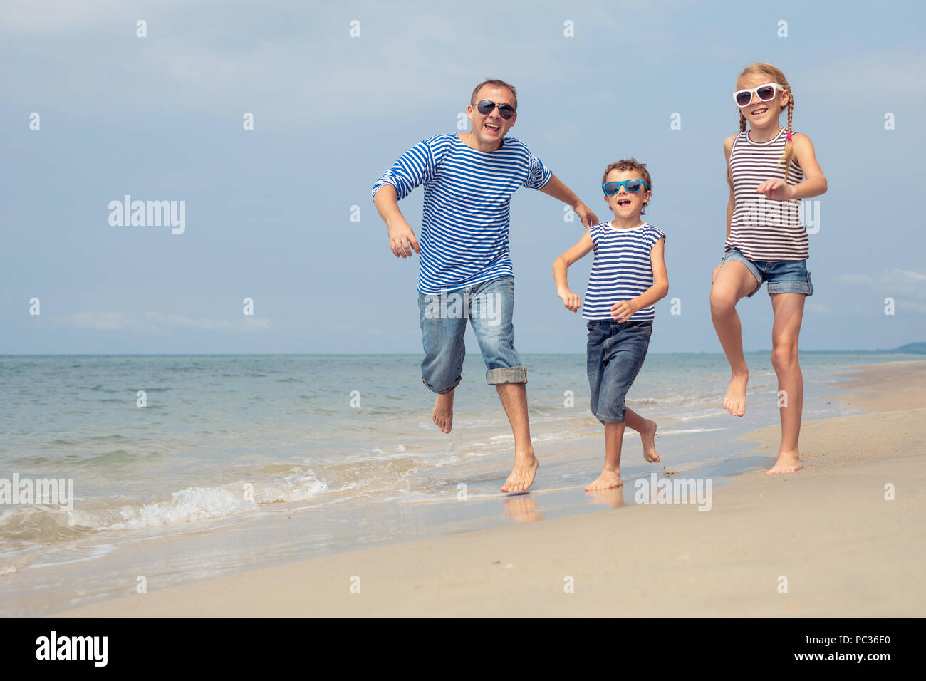 Father and kids playing on the beach at the day time. They are dressed in sailor's vests. Concept of sailors on vacation and friendly family. Stock Photo
