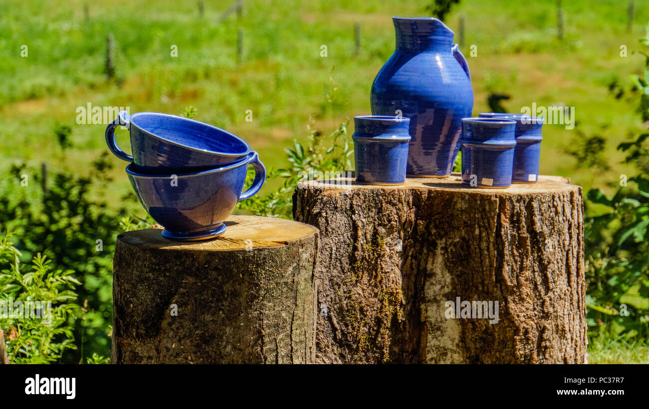blue pottery stacked and displayed outside on tree trunks for sale Stock Photo