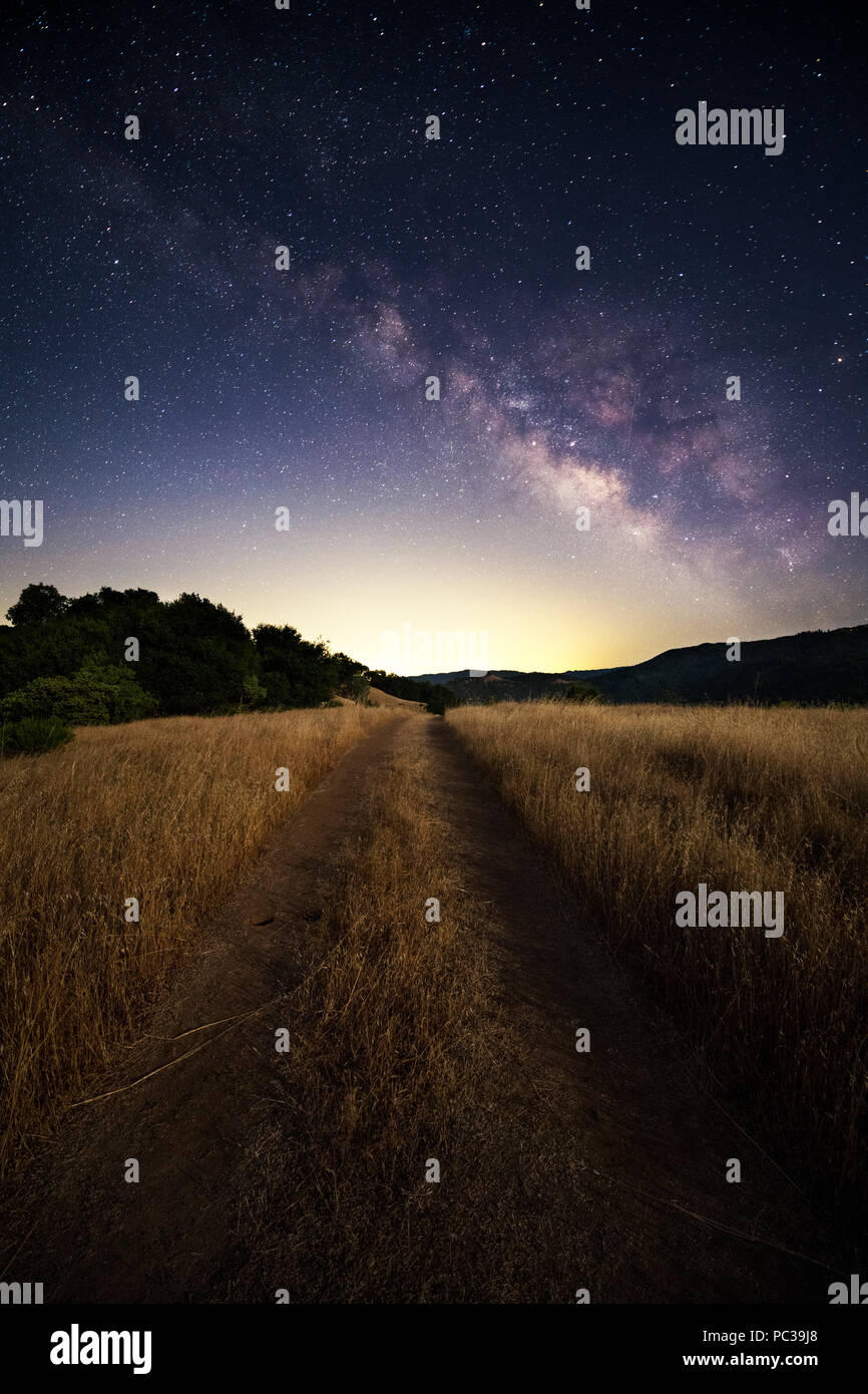 A dirt road travels through a field with the night sky, Milky Way and stars overhead near Lake Sonoma, California. Stock Photo