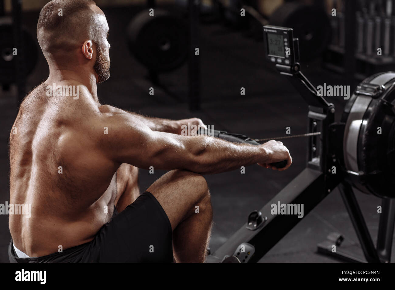 side view photo of shirtles man using th rowing machine while training in the sport center. health and free time concept Stock Photo