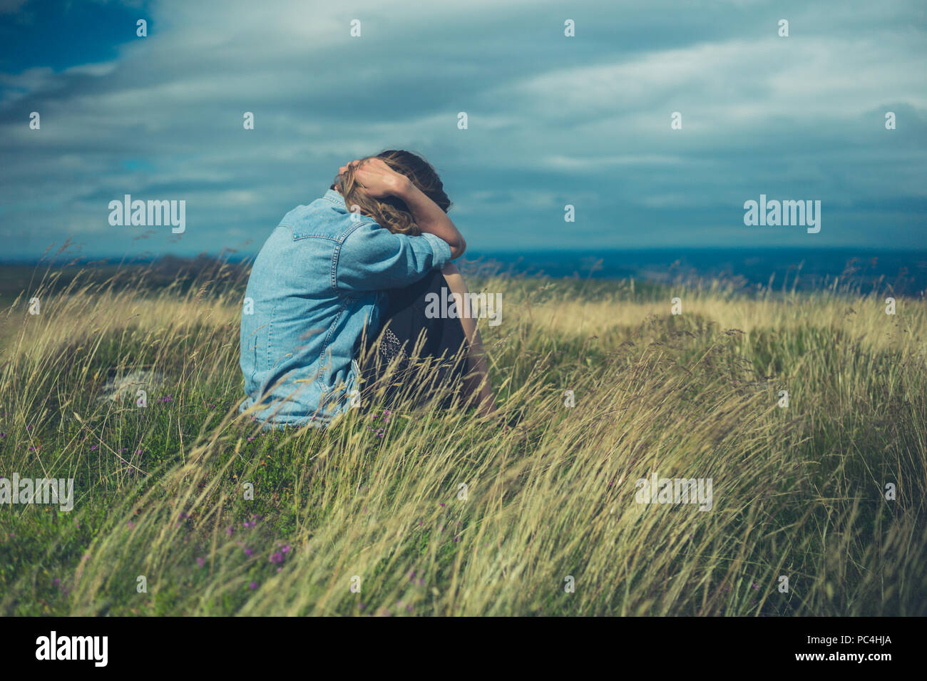 A sad woman is sitting in a field on a windy day Stock Photo