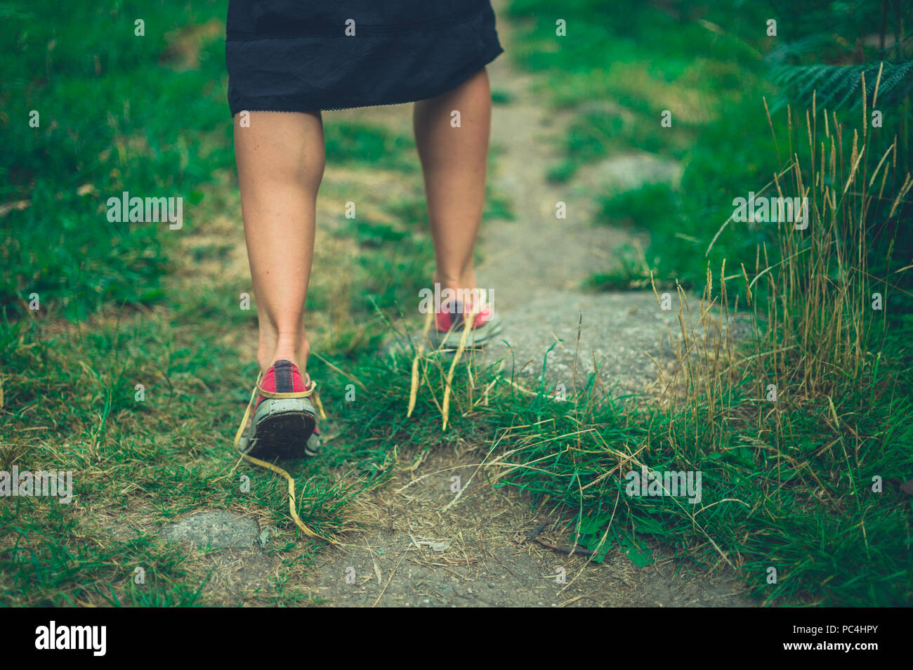 A young woman with undone shoe laces is walking in nature Stock Photo