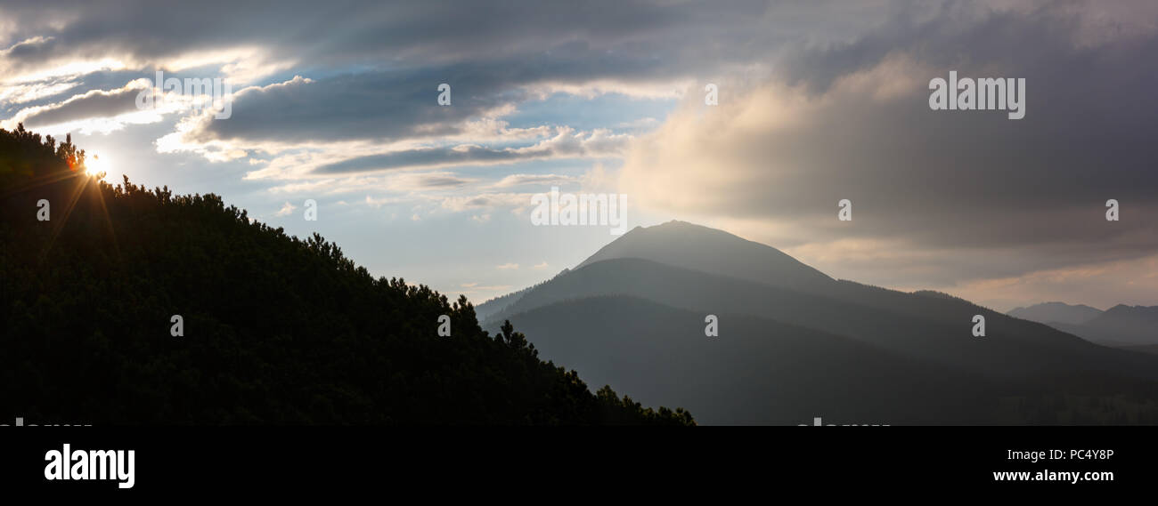 Last sun rays in evening sky with clouds above Syniak mountain. Summer sunset view from Homiak mountain, Gorgany, Carpathian, Ukraine. Stock Photo