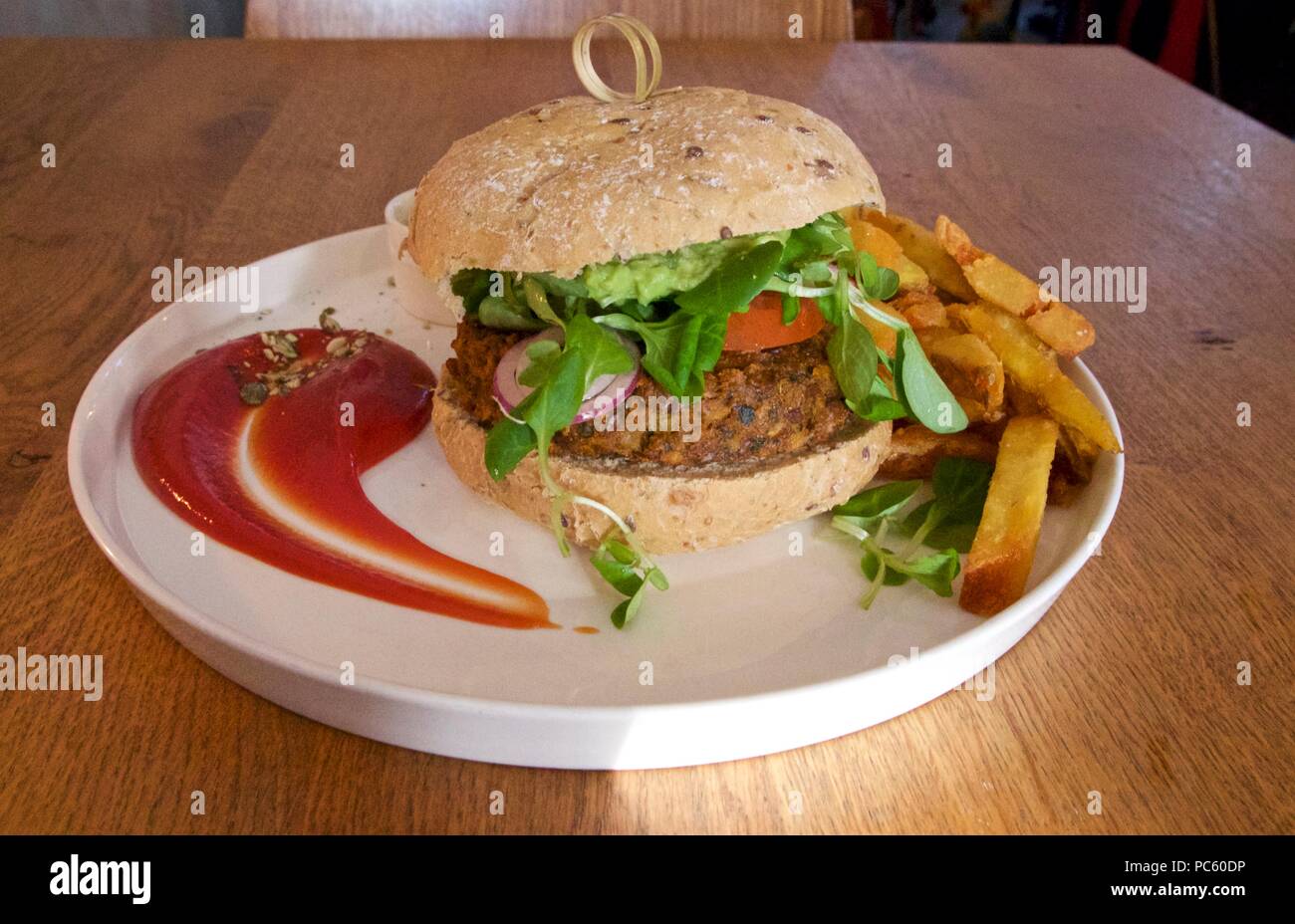 A meat-free, vegan meal of potato fries, ketchup and a seitan burger on a white plate Stock Photo