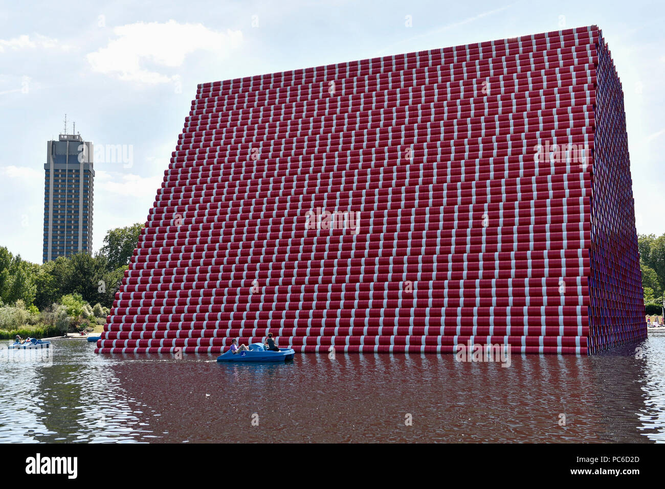 London, UK.  1 August 2018. UK Weather - People in pedal boats pass by 'The London Mastaba' on The Serpentine during warm weather in Hyde Park. The sculpture by artist Christo and Jeanne-Claude comprises 7,506 horizontally-stacked coloured barrels, in hues of red, blue, mauve and white, secured on a floating platform.  The geometric form takes inspiration from ancient mastabas from Mesopotamia and will be on display until 21 September 2018. Temperatures are forecast to increase back to the 30s in time for the weekend.  Credit: Stephen Chung / Alamy Live News Stock Photo