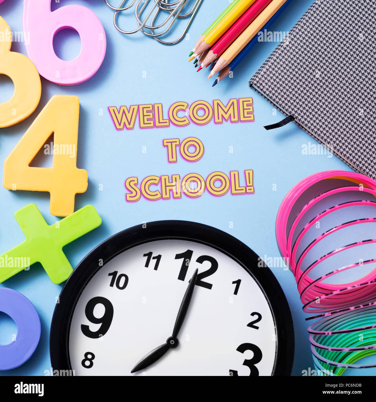 closeup of a clock, some pencil crayon of different colors, a notepad, some paper clips, some numbers of different colors and the text welcome to scho Stock Photo