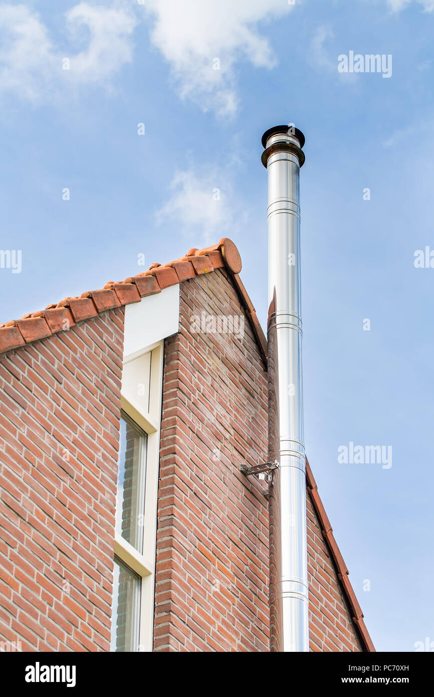 Metal chimney pipe on brick wall of home with blue sky Stock Photo