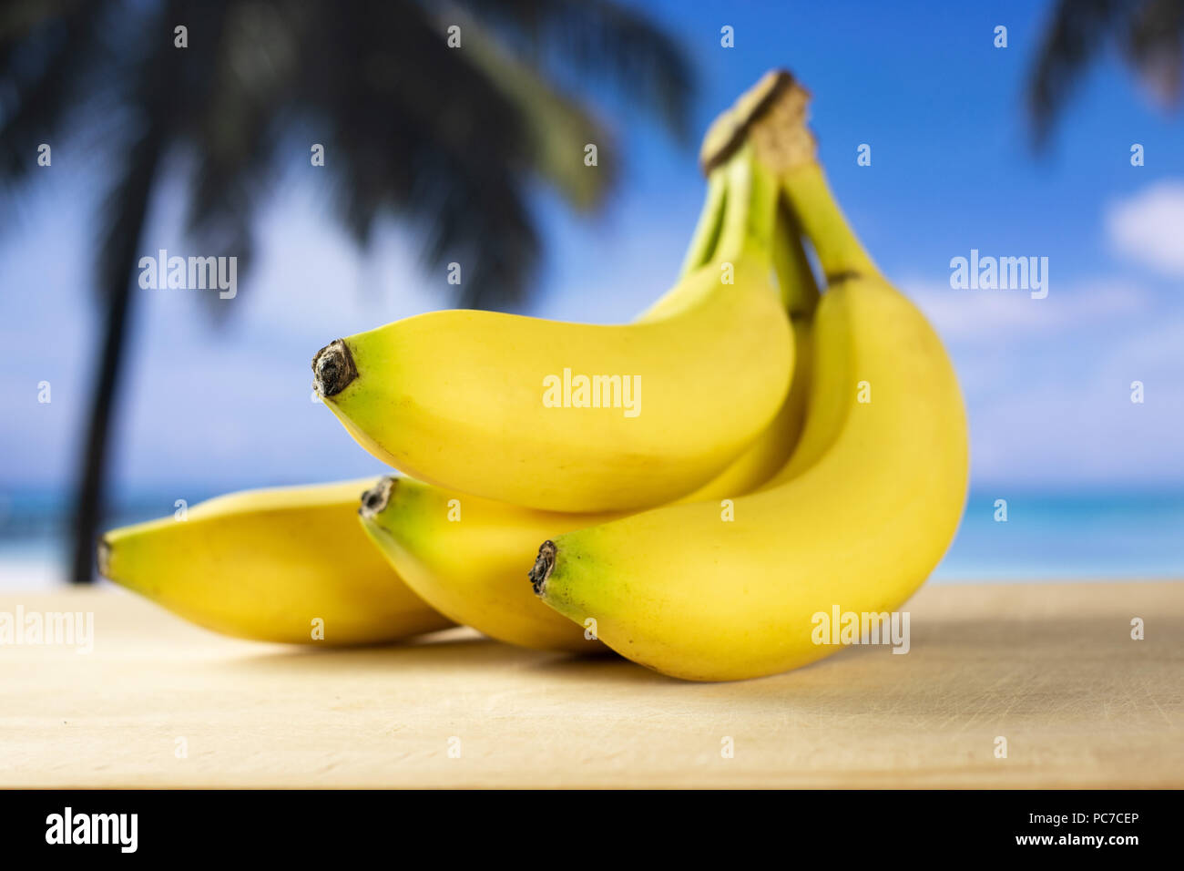 Group of four whole fresh yellow banana one cluster with palm trees on the beach in background Stock Photo