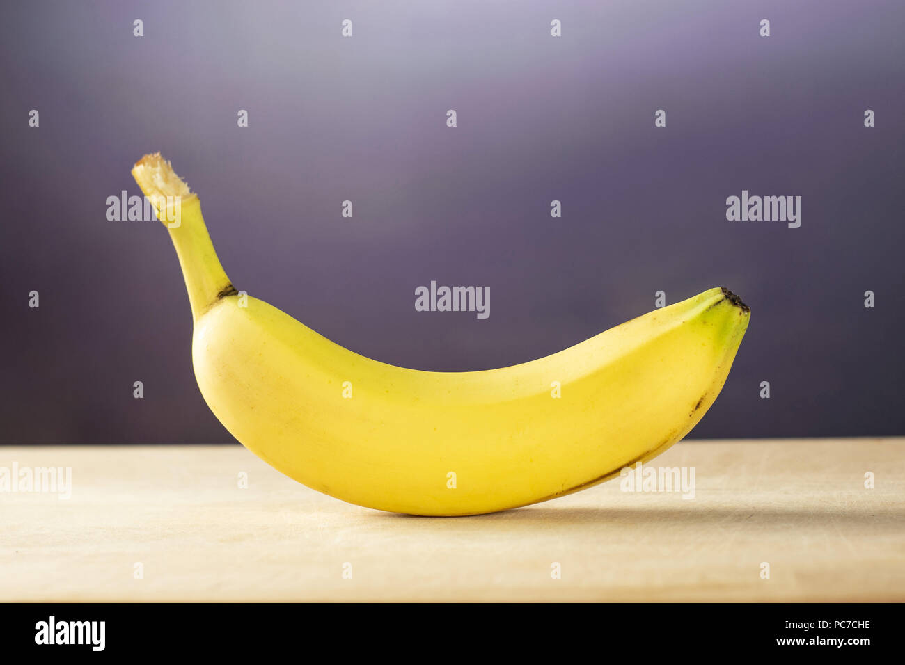 One whole fresh yellow banana with grey gradient behind Stock Photo