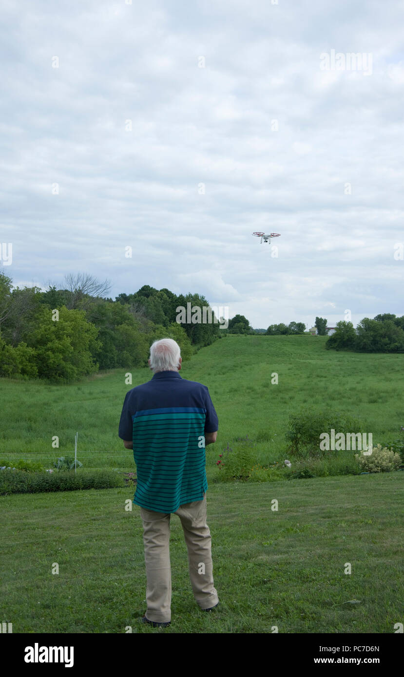 Man operating a dji Phantom Quadcopter Drone unmanned aerial vehicle in flight over open field. Stock Photo