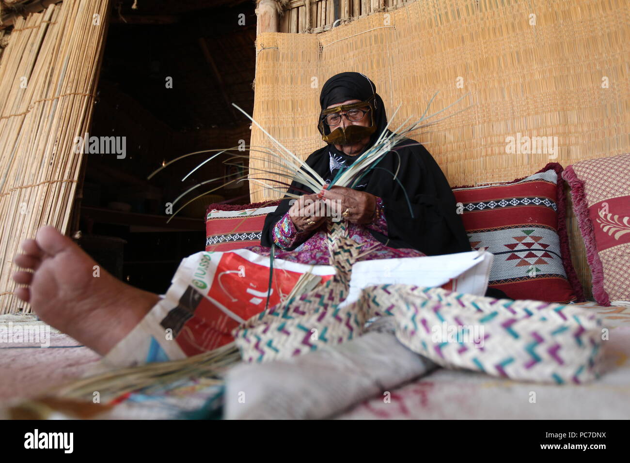 A UAE woman, sporting a metallic burqa with henna died fingers, weaves straw baskets and mats out of palm leaves at the heritage village in Fujairah. Stock Photo