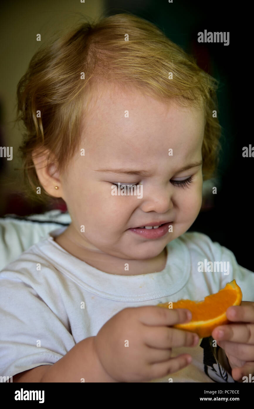Baby girl eating orange for the first time. Showing her funny reactions
